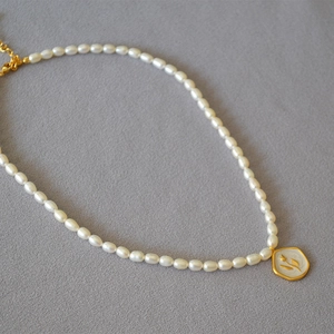 Detail of vintage freshwater pearl necklace with gold tulip relief on white enamel pendant