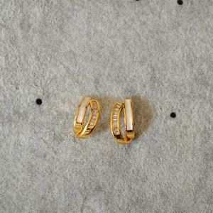 Close-up of C-shaped gold-plated earrings with zircon stones and white shell inlays