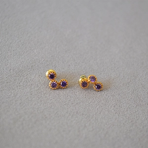 Detailed view of three-stone cluster earrings with purple cubic zirconia in gold plating