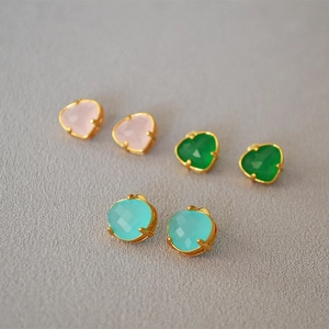Close-up of three pairs of heart-cut stud earrings in pink green and blue with gold plating