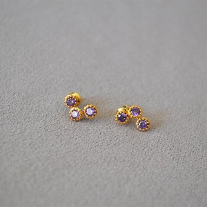 Macro shot of gold stud earrings featuring three sparkling purple cubic zirconia stones
