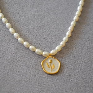 Detail of freshwater pearl necklace featuring a white enamel tulip relief gold pendant