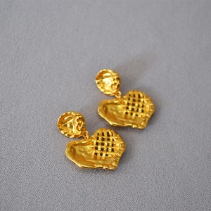 Dettaglio di orecchini a cuore in ottone dorato con trama martellata e design intrecciato
