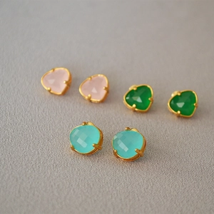 Detailed view of faceted gemstone earrings in pink, emerald green, and teal blue with gold plating