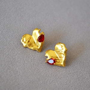 Macro view of gold lava heart earrings with red teardrop gems on grey fabric