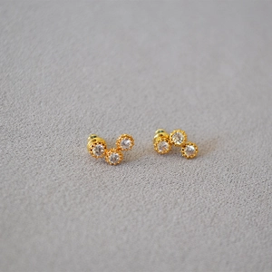 Detailed close-up of gold three-stone cubic zirconia studs with a textured bezel finish