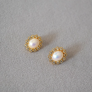 Detailed view of gold earrings with oval faux pearl and sparkling crystal wreath