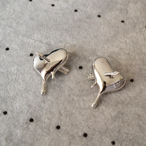 Détail de boucles d'oreilles cœur argenté fluide avec flèche sur plateau de velours