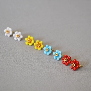 Detail showing four pairs of enamel camellia stud earrings in white, yellow, blue, and red