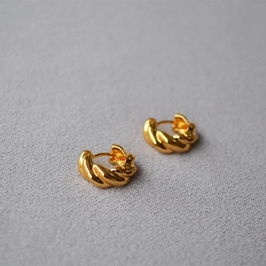 Detail of twisted croissant hoop earrings in gold plated brass on a textured background