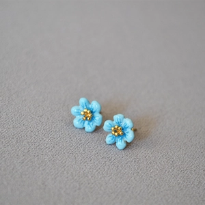 Close-up of light blue enamel camellia stud earrings with golden stamens on 925 silver pins