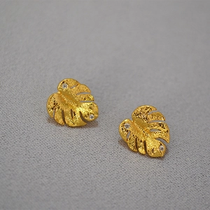 Golden Monstera leaf earrings with cubic zirconia inlay on elegant matte gray background