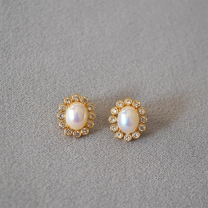 Detailed shot of gold earrings with oval faux pearl and sparkling zircon wreath