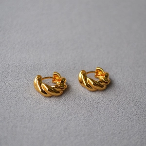 Macro detail of gold plated croissant twist hoop earrings with polished braided texture