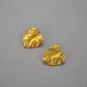 Macro shot of gold monstera leaf earrings with zircon inlays and hammered texture