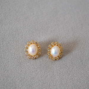 Detail of vintage oval faux pearl earrings with a sparkling zircon halo and gold setting