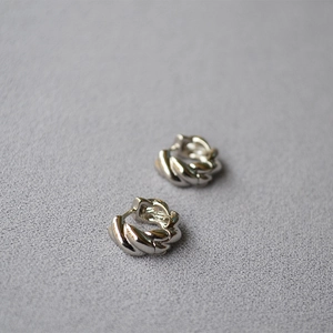 Detailed close-up of polished silver twist huggie earrings with spiral texture on grey surface