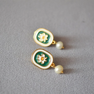 Macro shot of vintage enamel chamomile earrings with gold edges and freshwater pearl details
