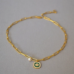 Detailed shot of golden paperclip chain necklace with green enamel daisy and pearl pendant