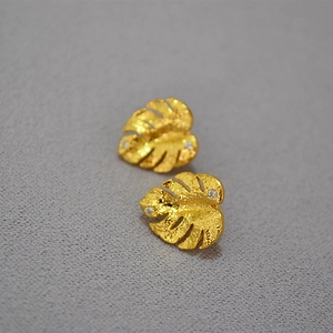 Close-up of golden monstera leaf earrings with zircon inlay and matte textured finish