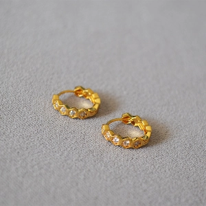 Détail de boucles d'oreilles créoles dorées hexagonales avec zircons étincelants