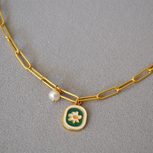 Macro shot of green enamel daisy pendant and pearl on golden paperclip chain