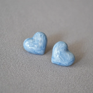 Macro detail of heart earrings with blue and white marble texture on a grey background