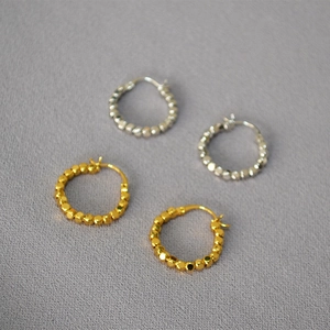 Détail de boucles d'oreilles créoles facettées en or et argent sur tissu gris