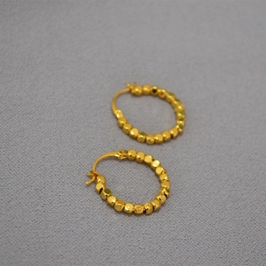 Boucles d'oreilles créoles à perles facettées en laiton doré, vue à 45 degrés sur gris