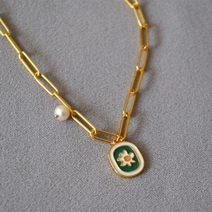 Detailed close-up of a gold paperclip chain necklace with green enamel daisy pendant