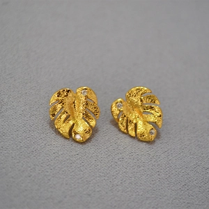 Macro shot of gold Monstera leaf earrings with fine matte texture and sparkling zircon