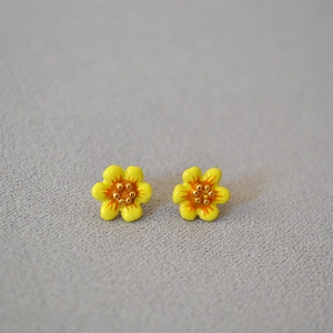 Macro view of handmade yellow enamel camellia flower stud earrings with gold stamen detail