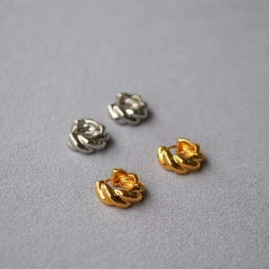 Detail of chunky twisted croissant hoop earrings in polished gold and silver finish