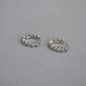Gros plan de boucles d'oreilles créoles hexagonales argentées avec motif nid d'abeille