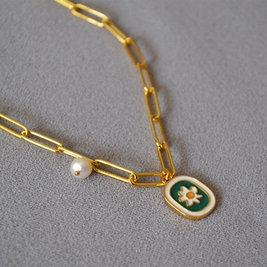 Close-up of gold paperclip chain necklace with pearl and green daisy enamel pendant