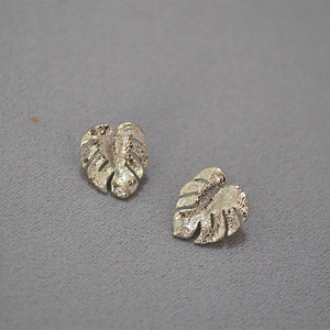 Macro detail of silver monstera leaf earrings with tiny zircon stones and brushed texture