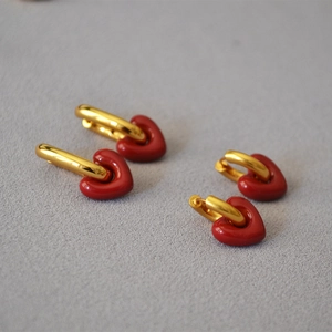 Detail view of red enamel heart charms on gold U-shaped earrings on grey background