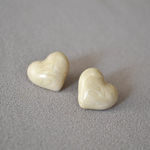 Macro shot of heart-shaped cream marble earrings on a grey textured background
