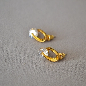 Detailed close-up of a golden earring with a sparkling round zircon in an irregular arc frame