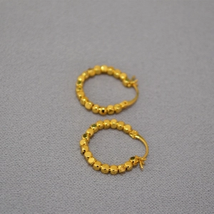 Détail de boucles d'oreilles créoles dorées avec perles facettées et fermoir à charnière