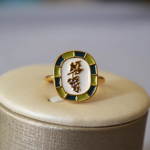 Macro detail of enamel ring with gold vine pattern and green blue geometric border