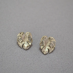 Macro shot of gold monstera leaf earrings with zircon pavé details on dark texture