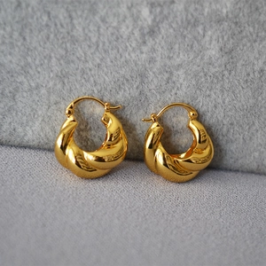 Détail macro des boucles d'oreilles torsadées dorées sur fond de tissu gris texturé