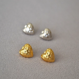 Macro shot of hammered heart-shaped stud earrings in gold and silver textured metal