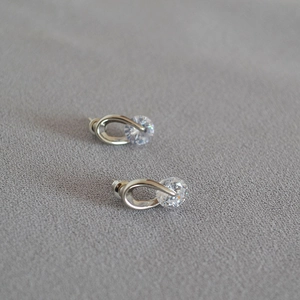 Macro shot of silver oval earrings with sparkling cubic zirconia on grey fabric