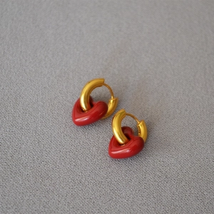 Detail of gold U-shaped hoop earrings with red enamel heart pendants on a textured surface