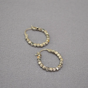 Boucles d'oreilles créoles minimalistes en perles argentées sur un fond en tissu gris