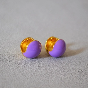 Detail of purple enamel huggie earring with polished gold-plated finish on textured surface