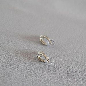 Detailed view of silver stud earrings with round clear zircon on grey fabric texture