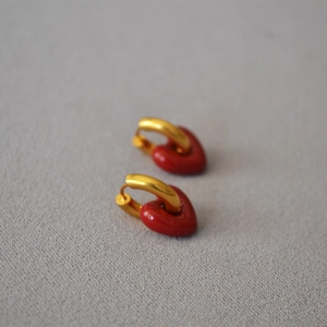 Close-up of heart charm earrings with red enamel finish and golden metal hoops